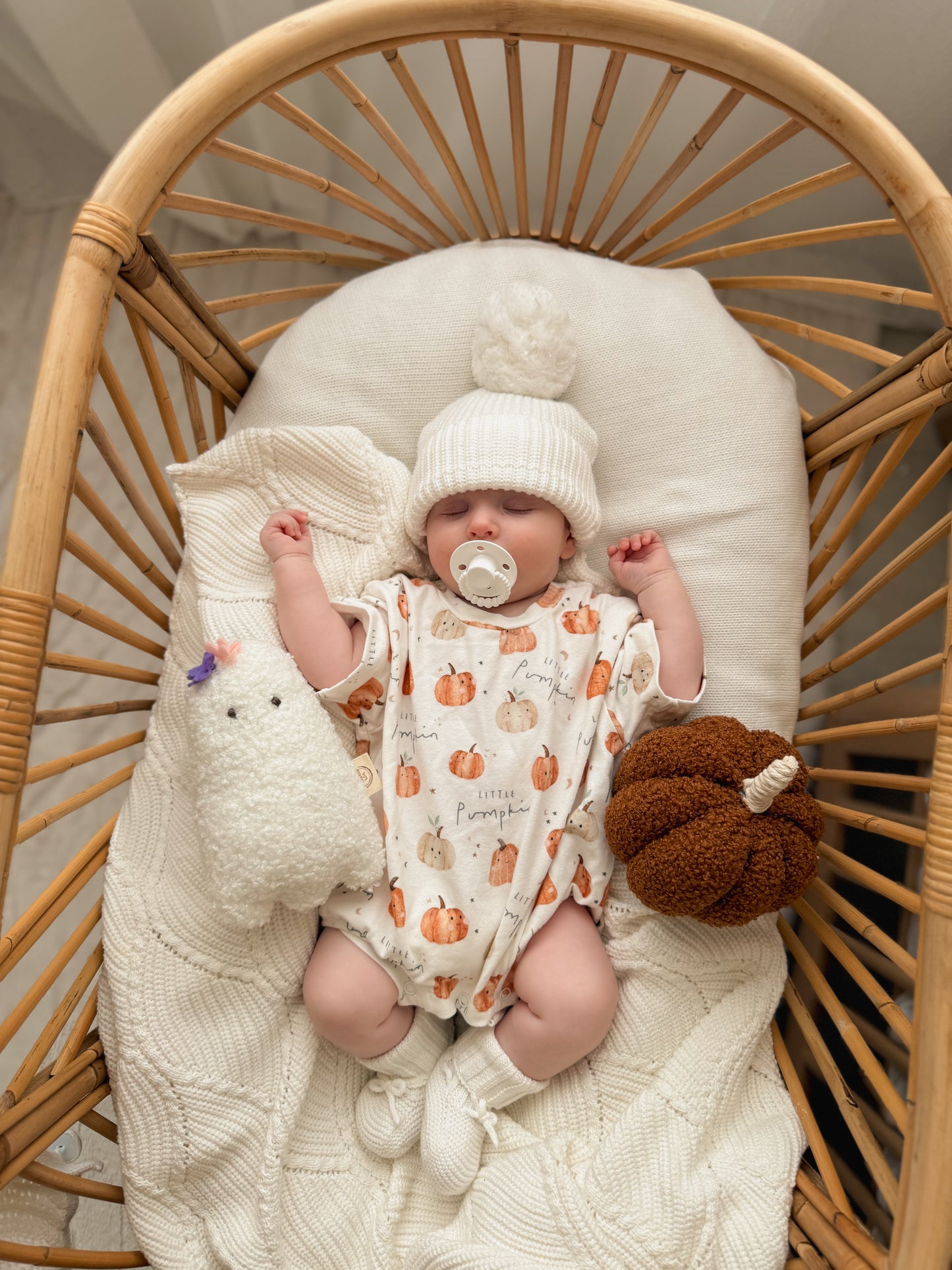Baby in a crib with a white blanket and pumpkin-patterned outfit
