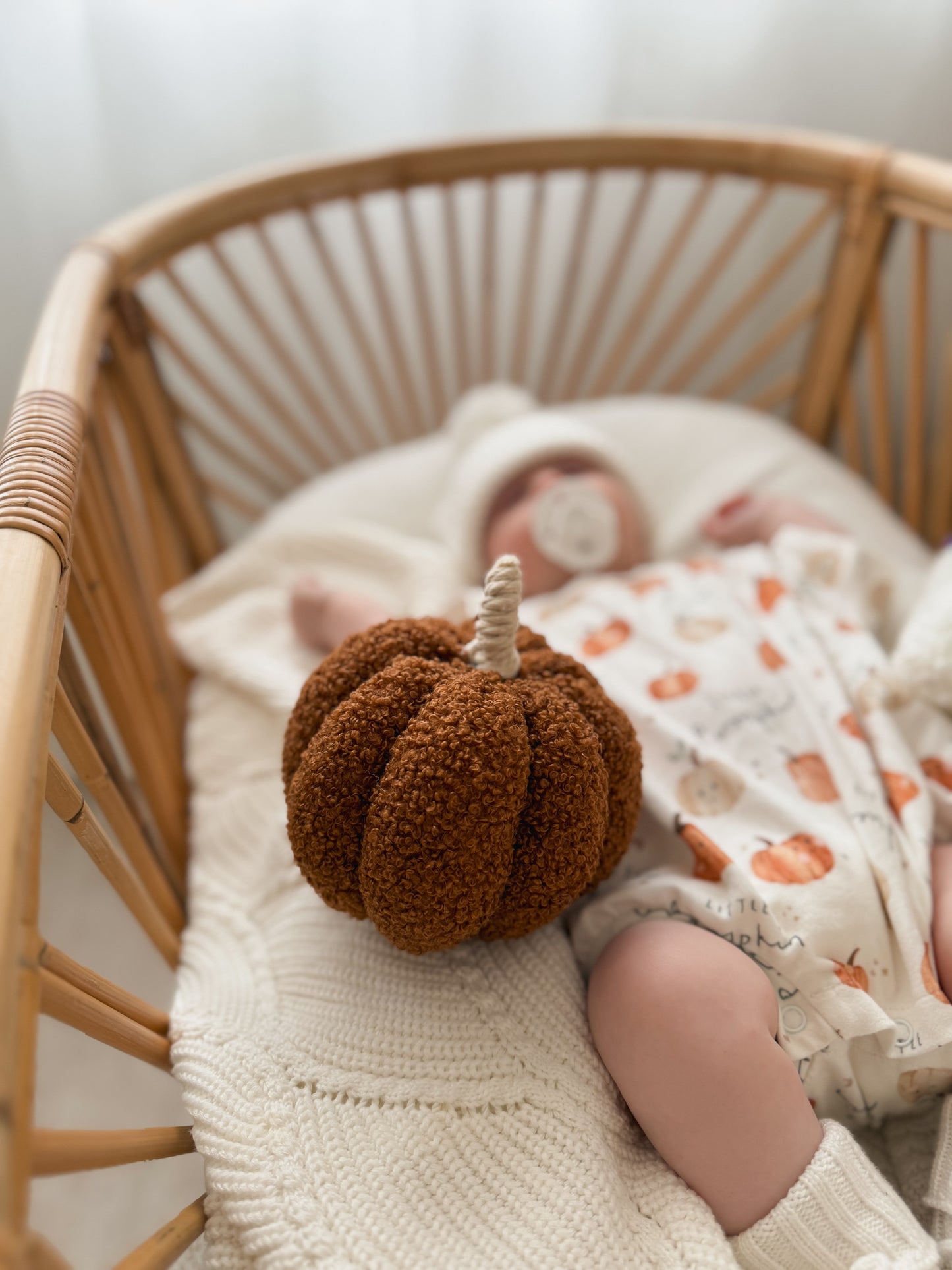 Baby sleeping in a crib with a brown plush pumpkin toy