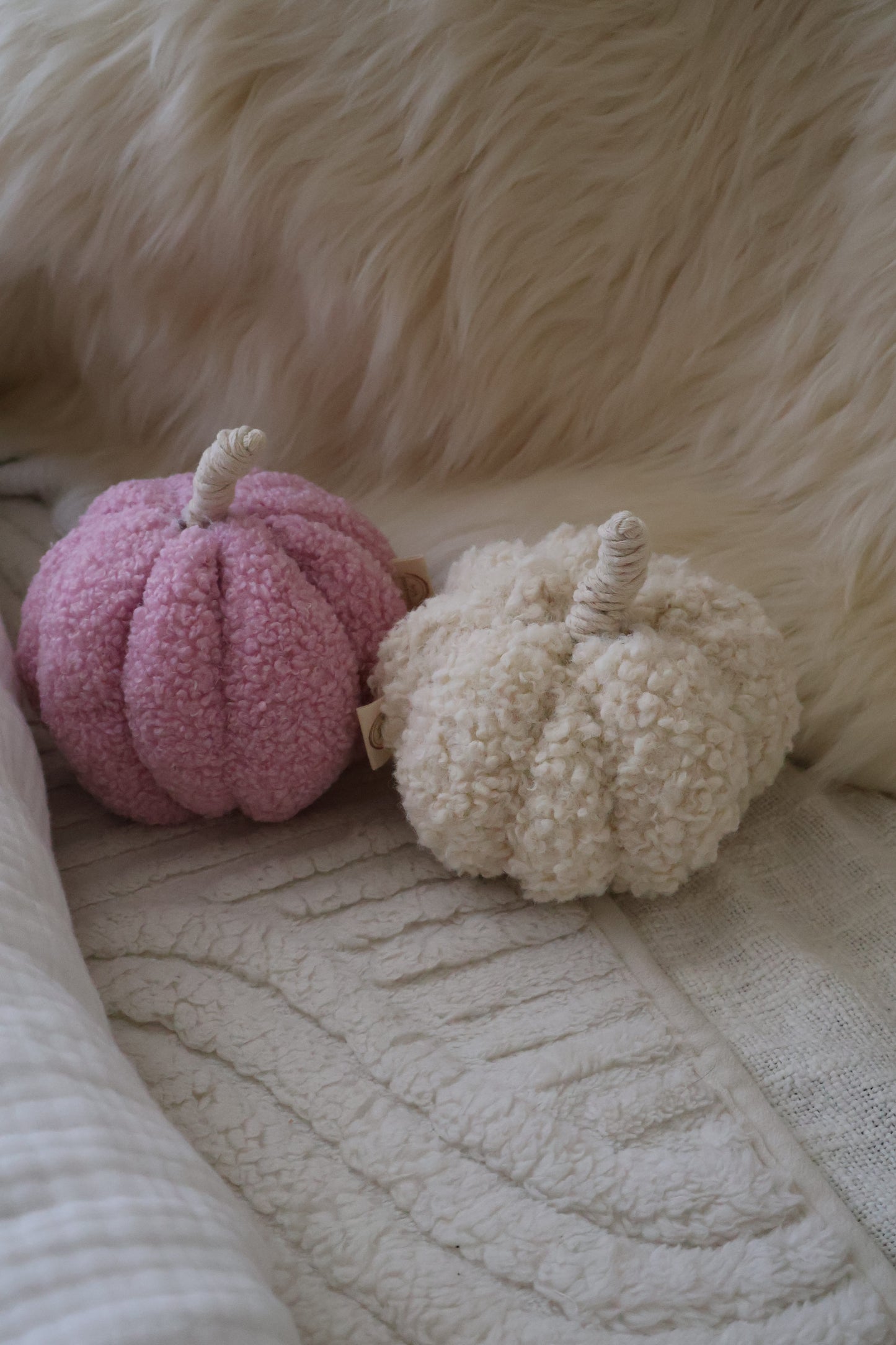 Two soft, plush pumpkins in pink and beige on a textured surface.