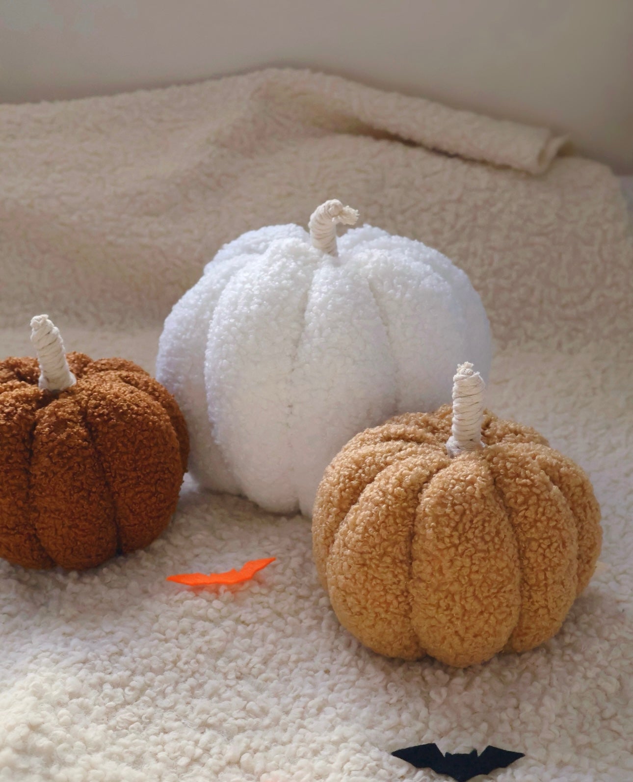Three textured pumpkins in brown, white, and beige on a textured surface.