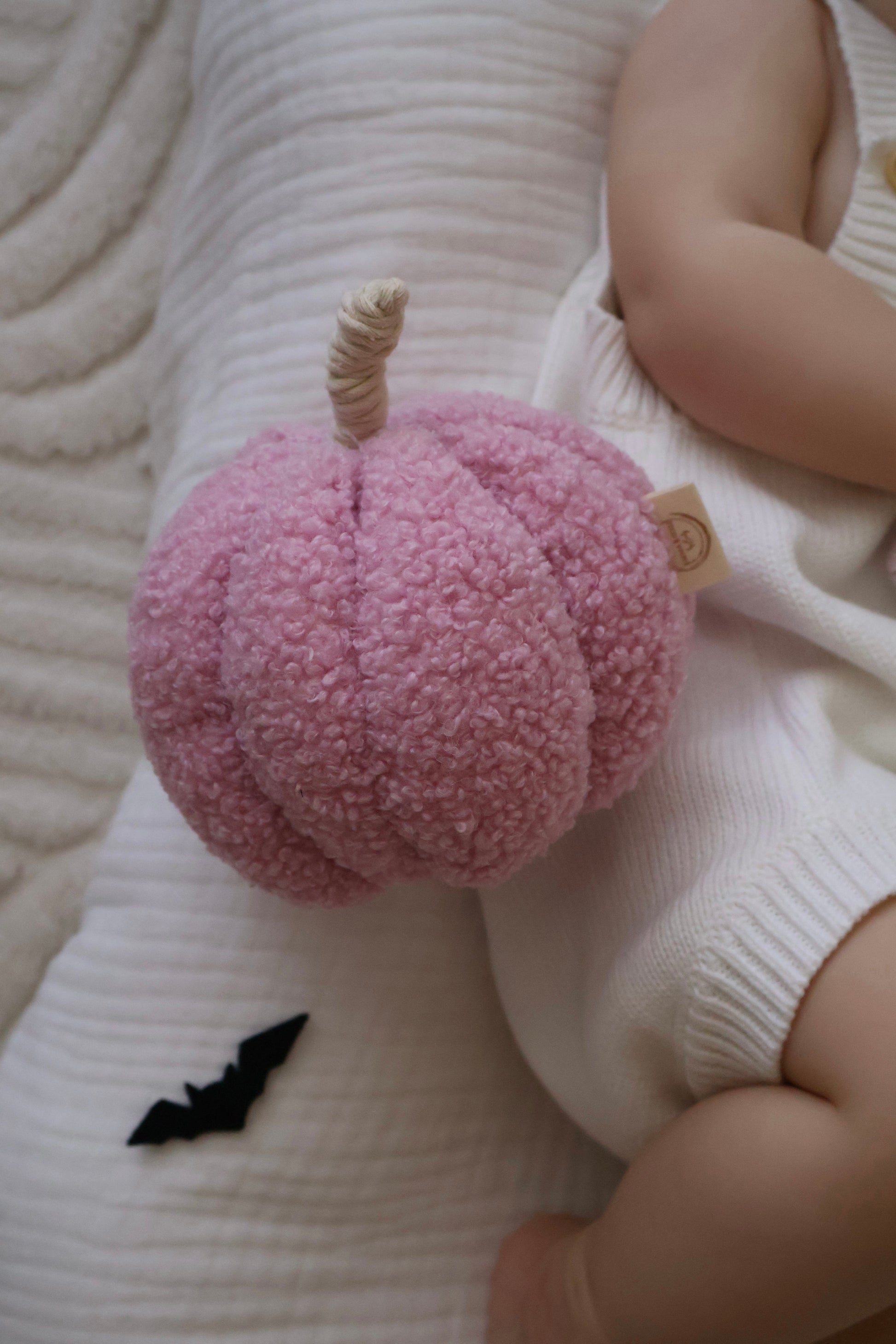 Pink plush toy resembling a pumpkin held by a child on a textured surface