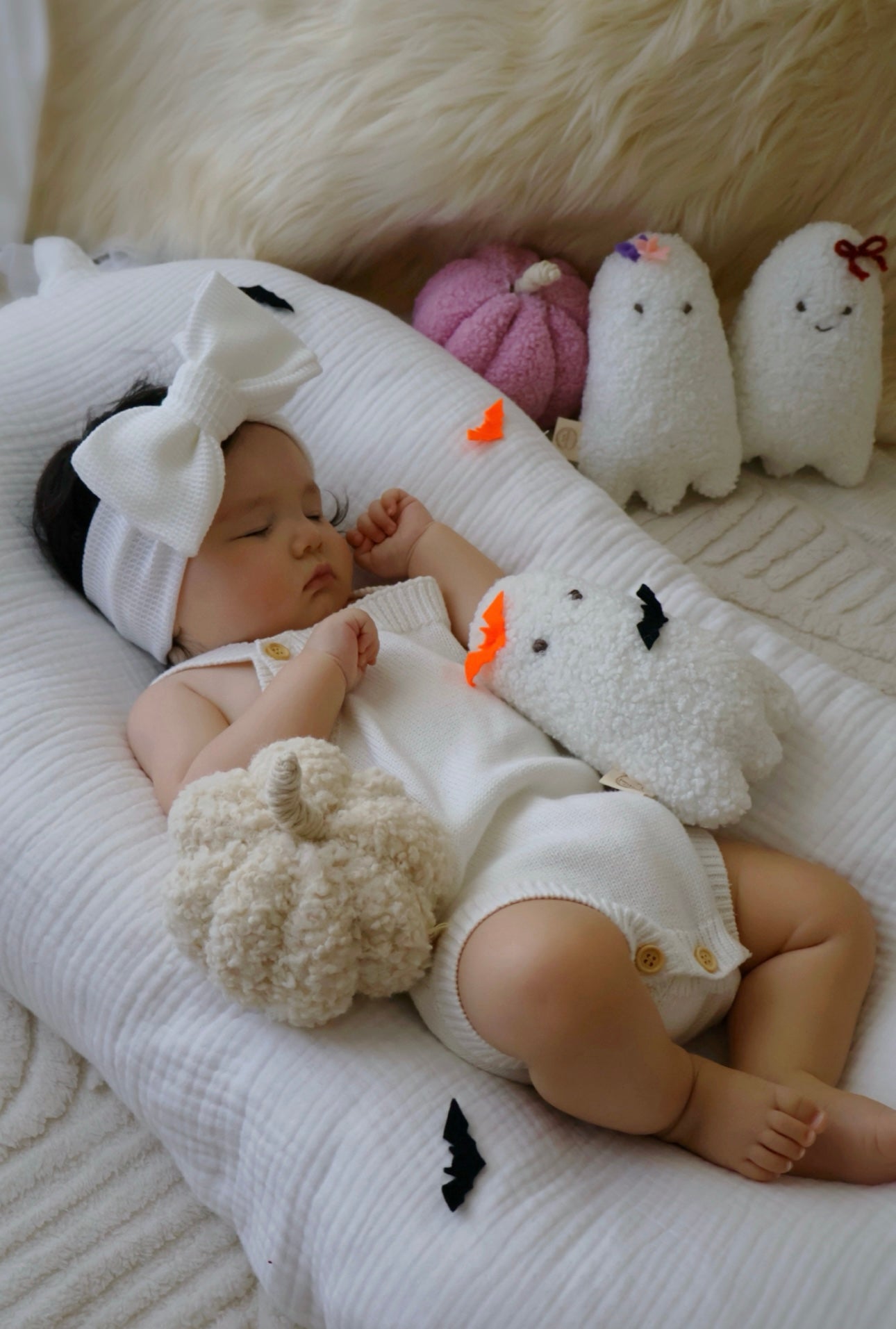 Baby lying on a white blanket with plush toys in the background